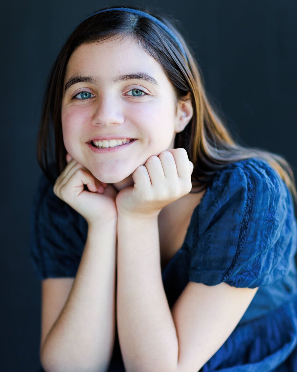 Headshot of a girl in blue dress with her head in her palms.