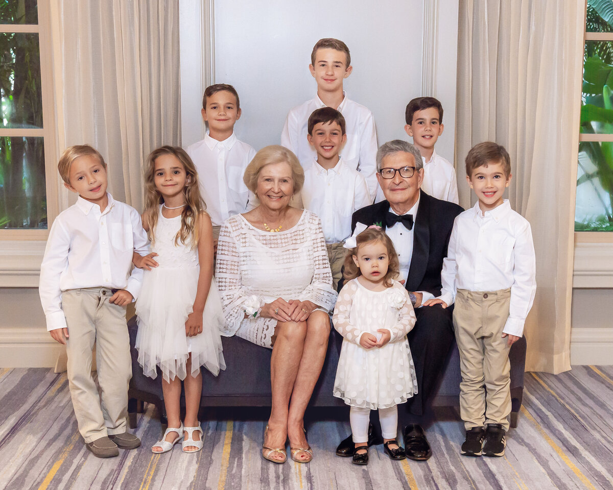 grandparents seated on a couch with many grandkids standing around them smiling