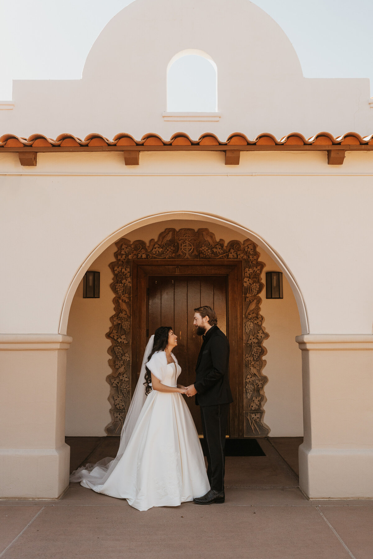 A newlywed couple with their arms around each other smiling at each other 