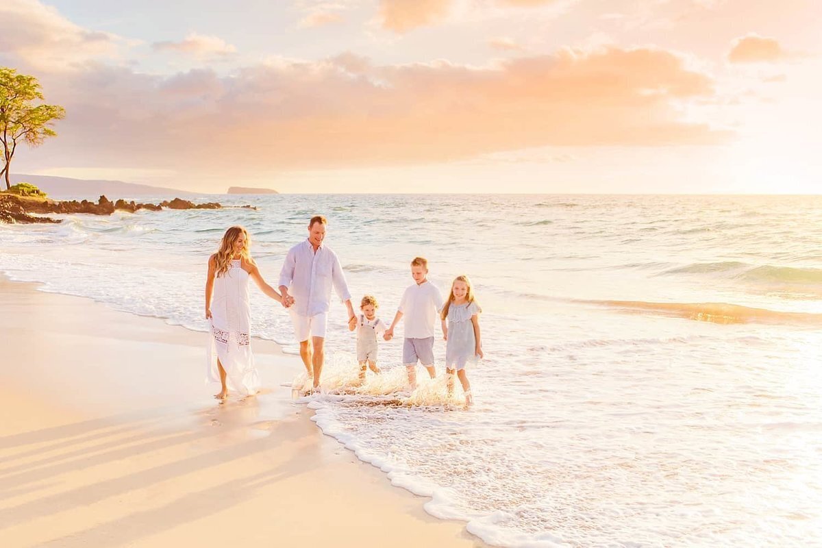 Family of five with three young kids holding hands and photographed on the beach in Wailea at sunset next to the ocean