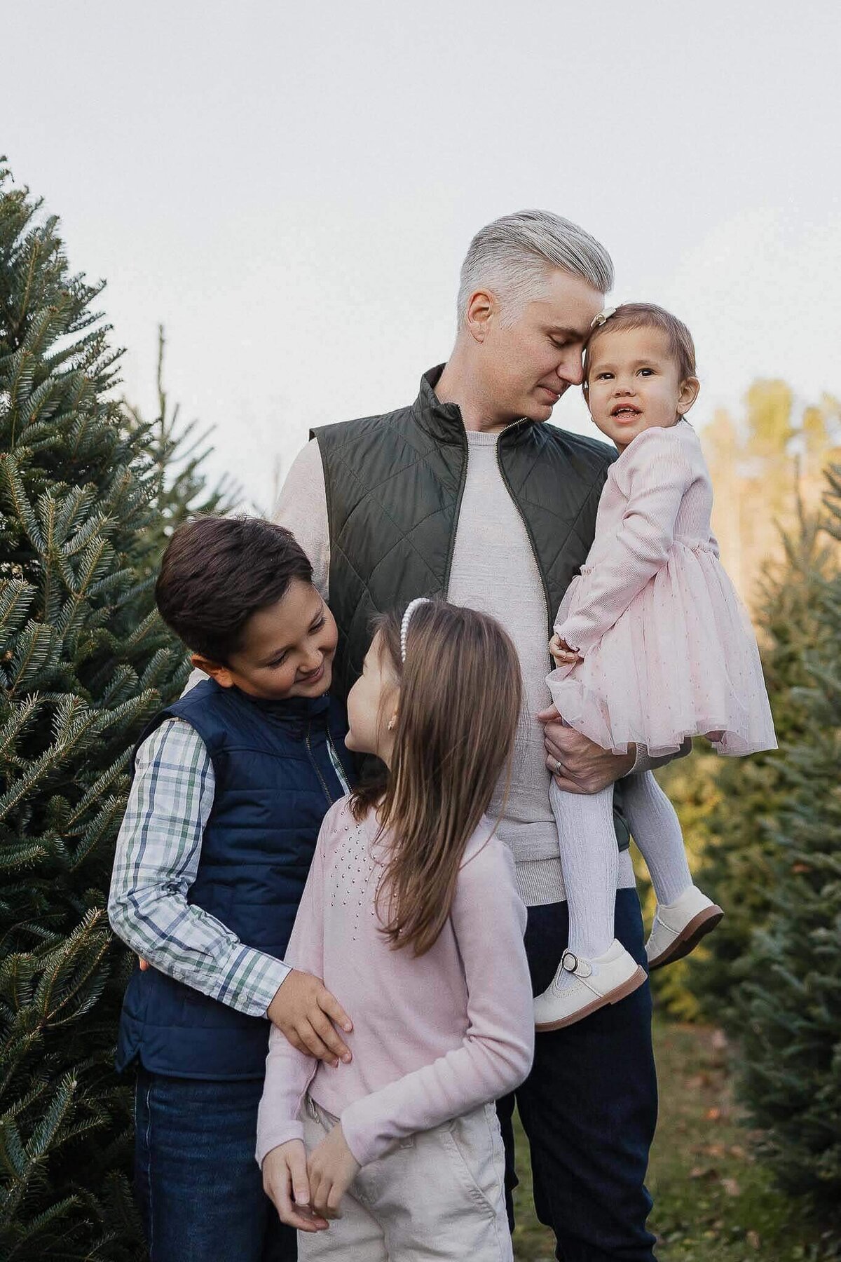 Dad snuggling with kids during Christmas mini session at Sugar Pines Tree Farm in Chesterland, Ohio.