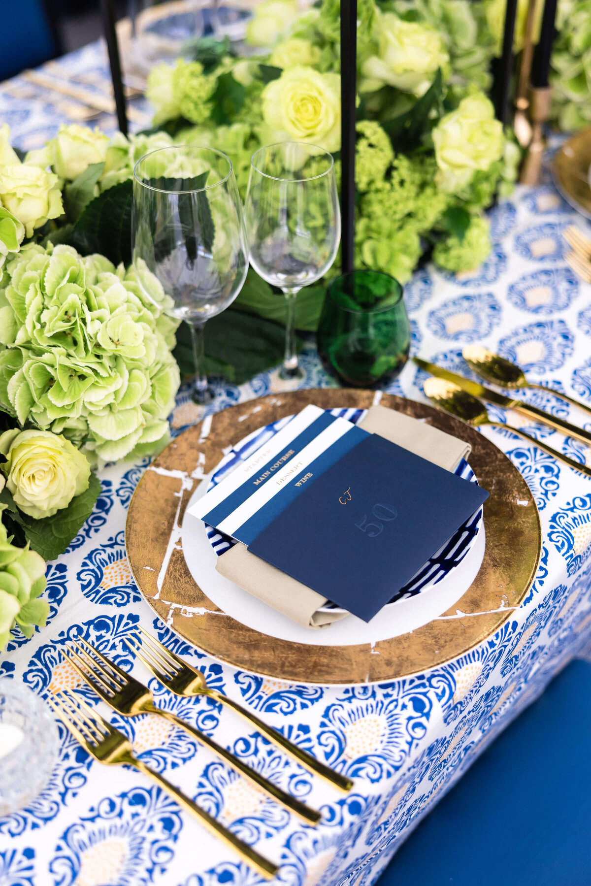 lime green flowers along the centre of a dinner table laid with blue patterned linen and gold charger plates topped with a blue menu for a birthday party