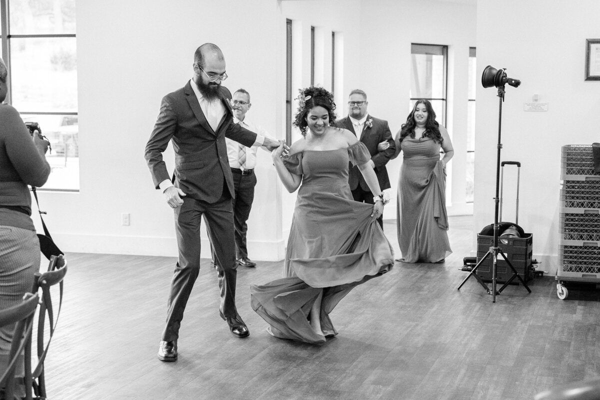 black and white of bridesmaid and groomsman dancing into reception