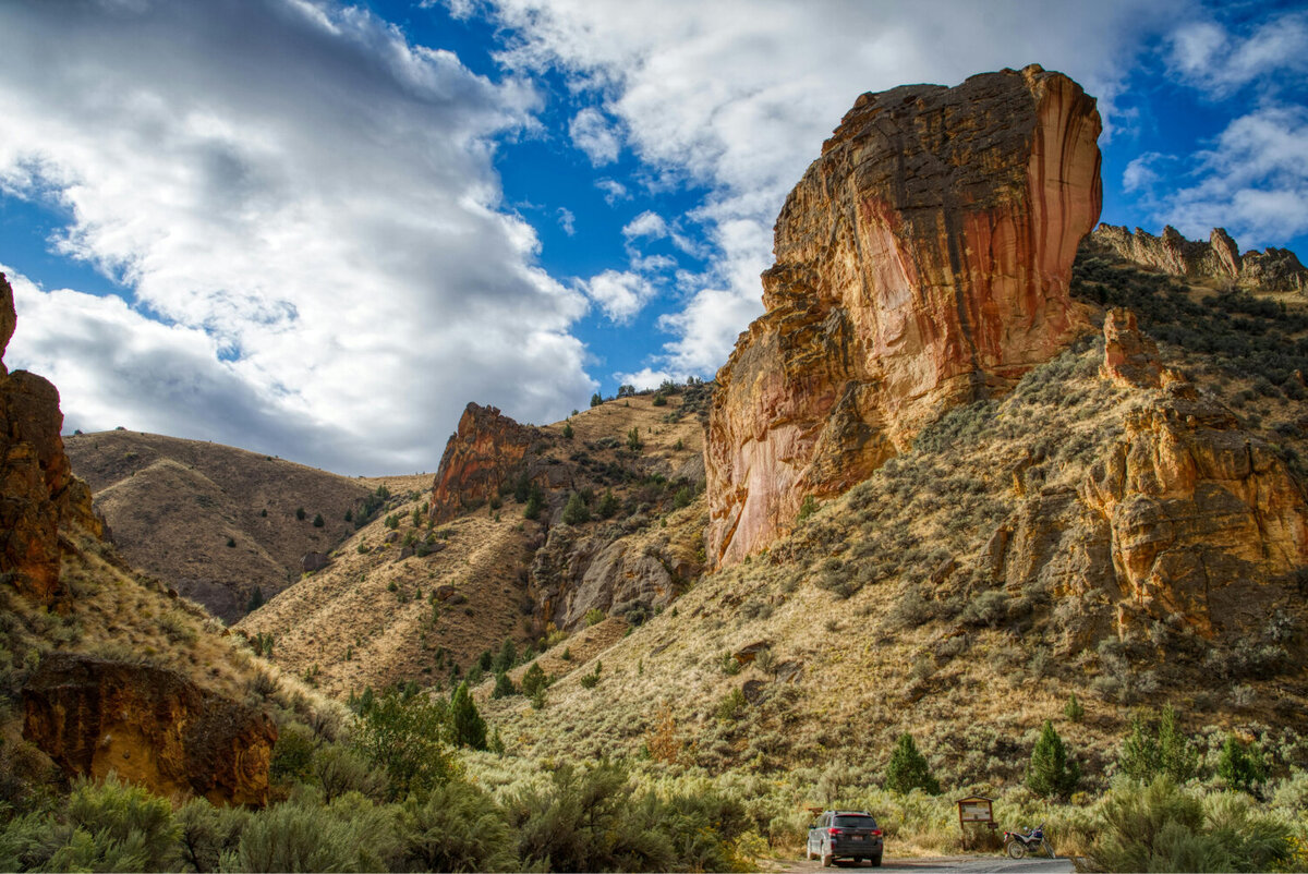Landscape photo of crumbly rock structures that make up steep slopes with greenery and trees around and below.