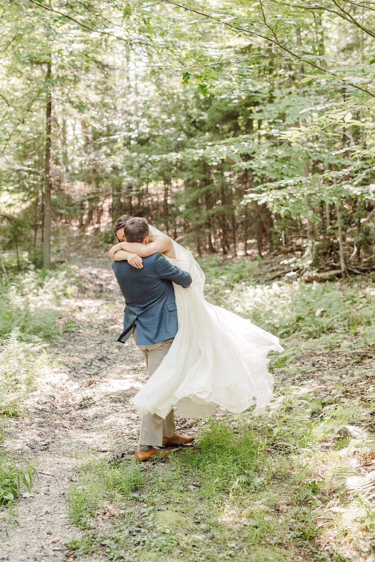 A photograph of a bride picking up and twirling his bride on a wooded trail in Stowe Vermont