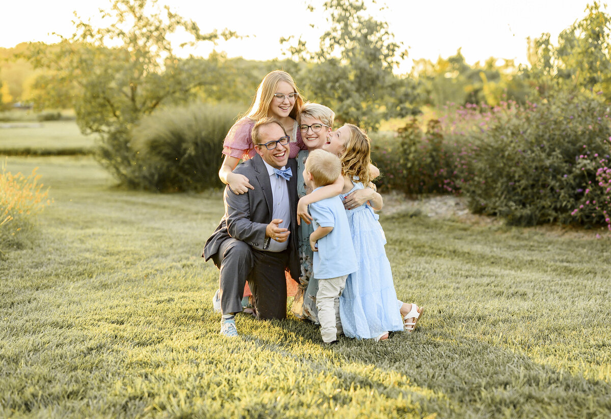 Parents with their three children snuggled together on a grassy field at sunset during a Kansas City family photography session.