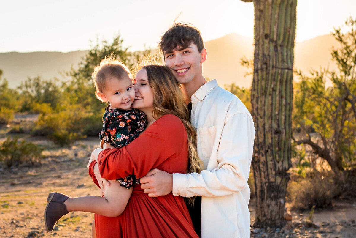 parents smiling, hugging young daughter during maternity session. Photographed by Cactus & Pine Photography