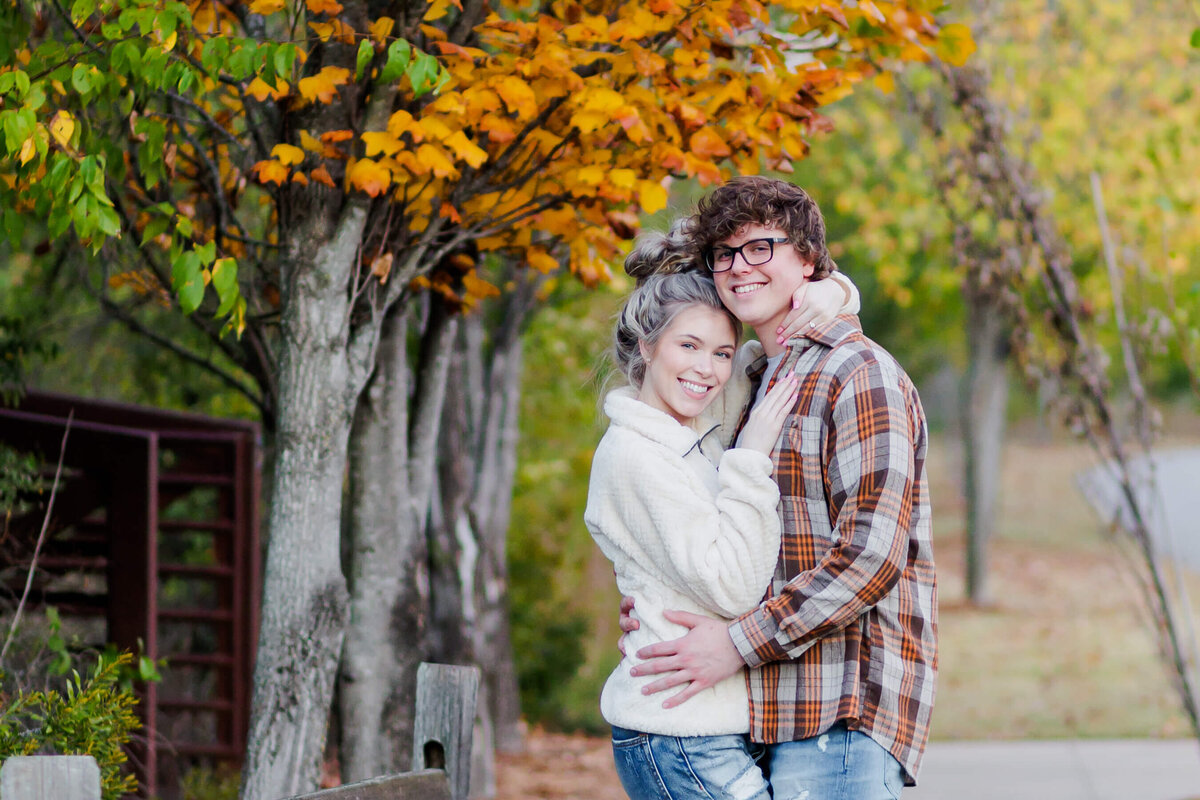 An engaged couple poses in front of an orange leaf tree in Conway, AR.