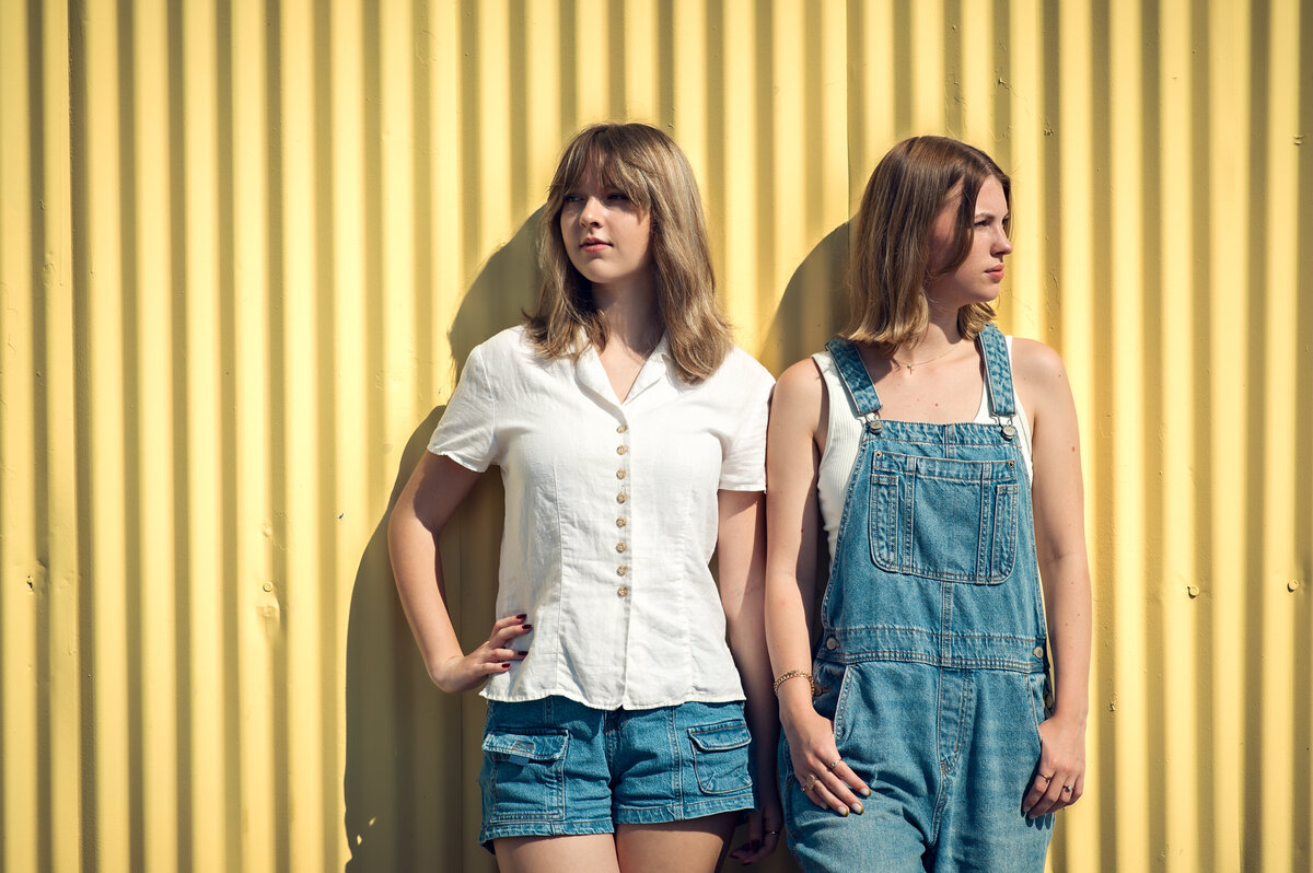 two high school senior girls leaning up against yellow wall in downtown winter garden