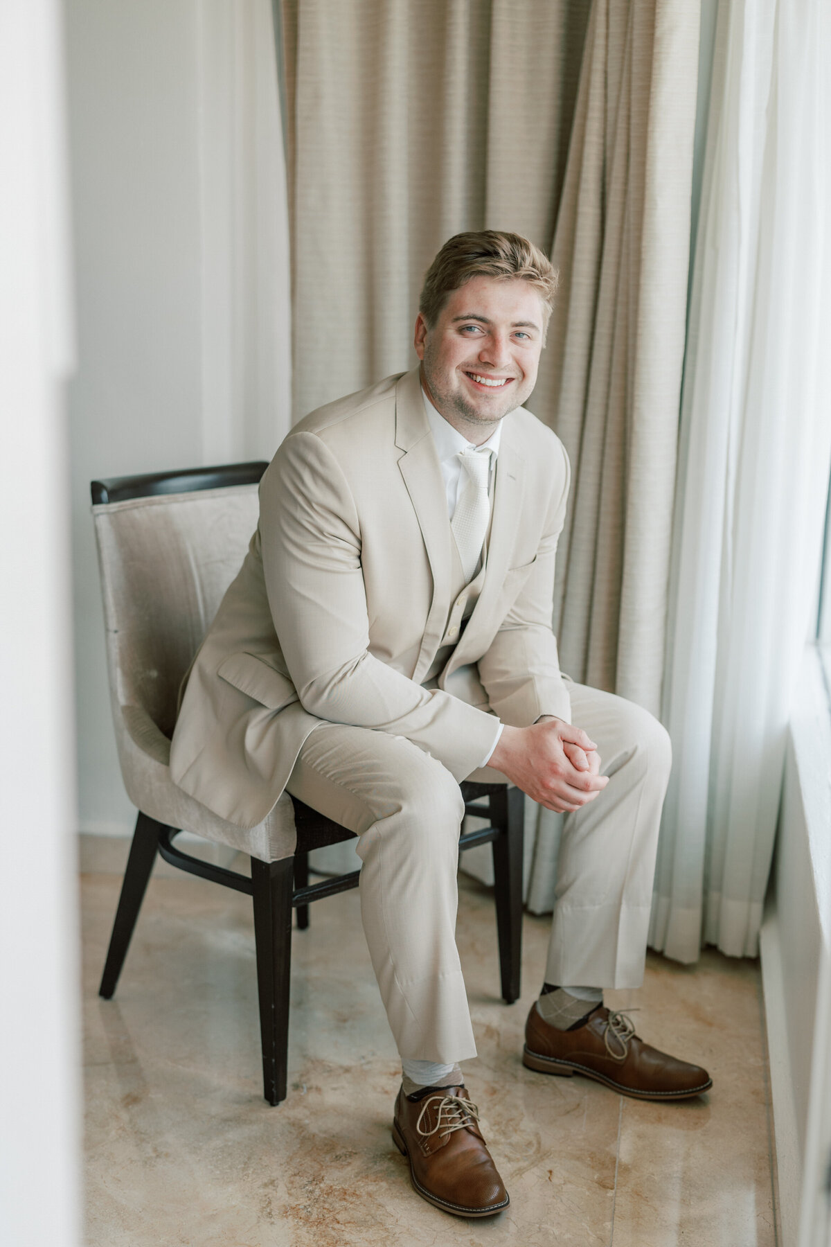 Groom smiling while seated near a window in Cancun resort, photographed by Philadelphia wedding photographer.