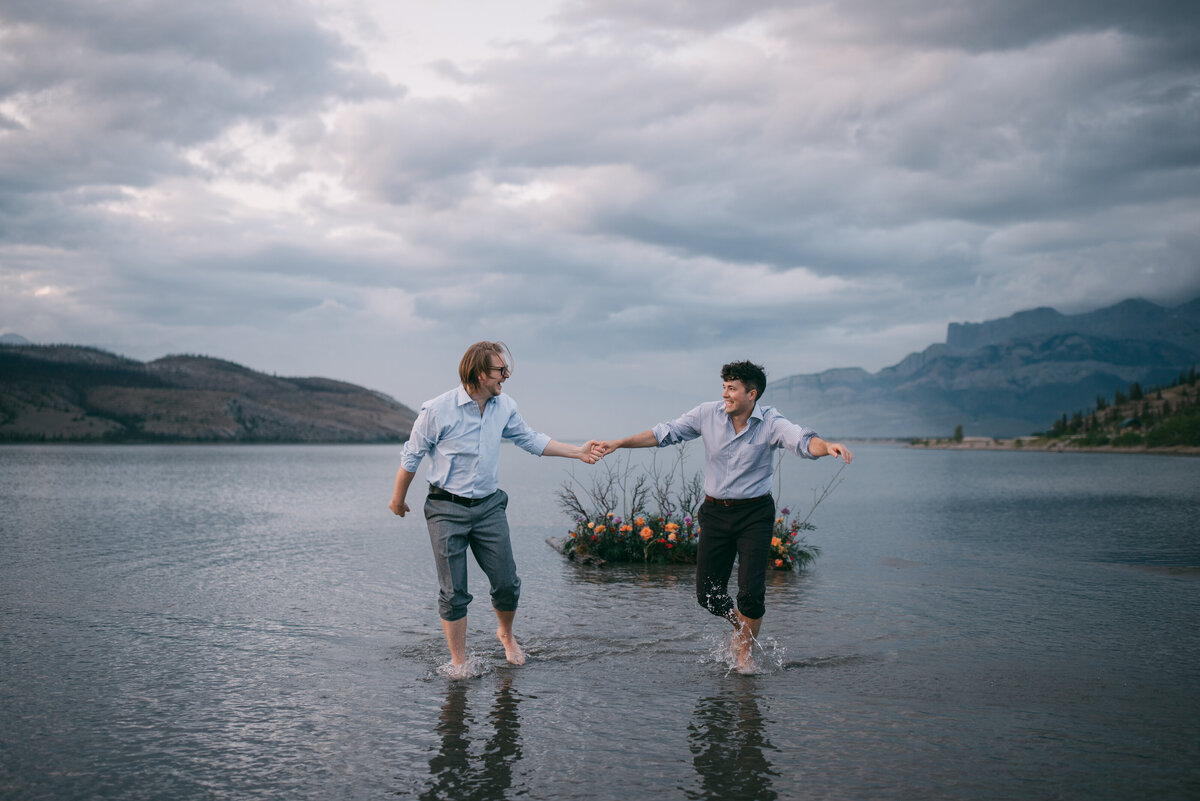 A couple holding hands and walking through water during as they elope in Jasper.