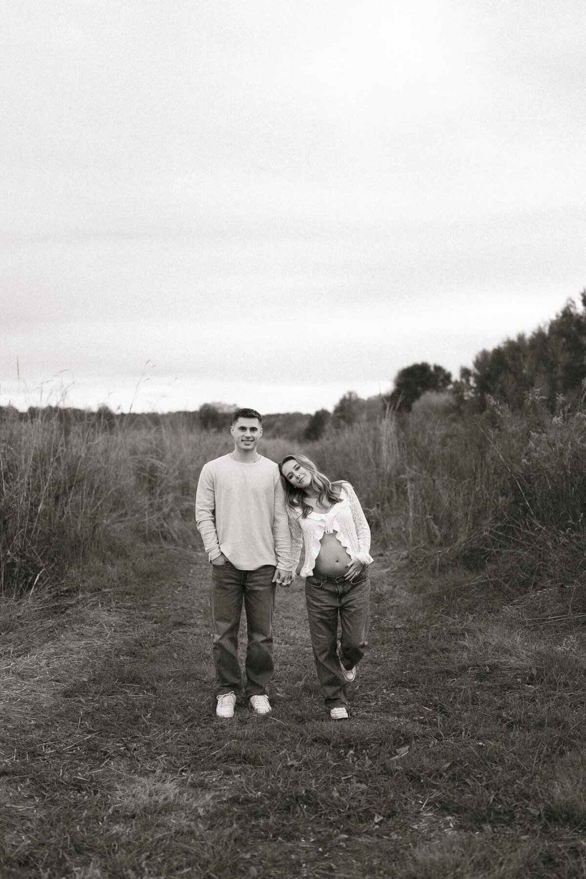 man and pregnant woman hold hands in field at seven islands state birding park near knoxville tennessee