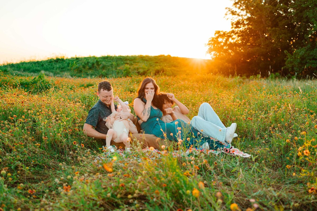 The expecting family is captured in the mountain setting, surrounded by yellow flowers. They are dressed in coordinated blue jean outfits, highlighting their joyful anticipation and the natural beauty of the scene.