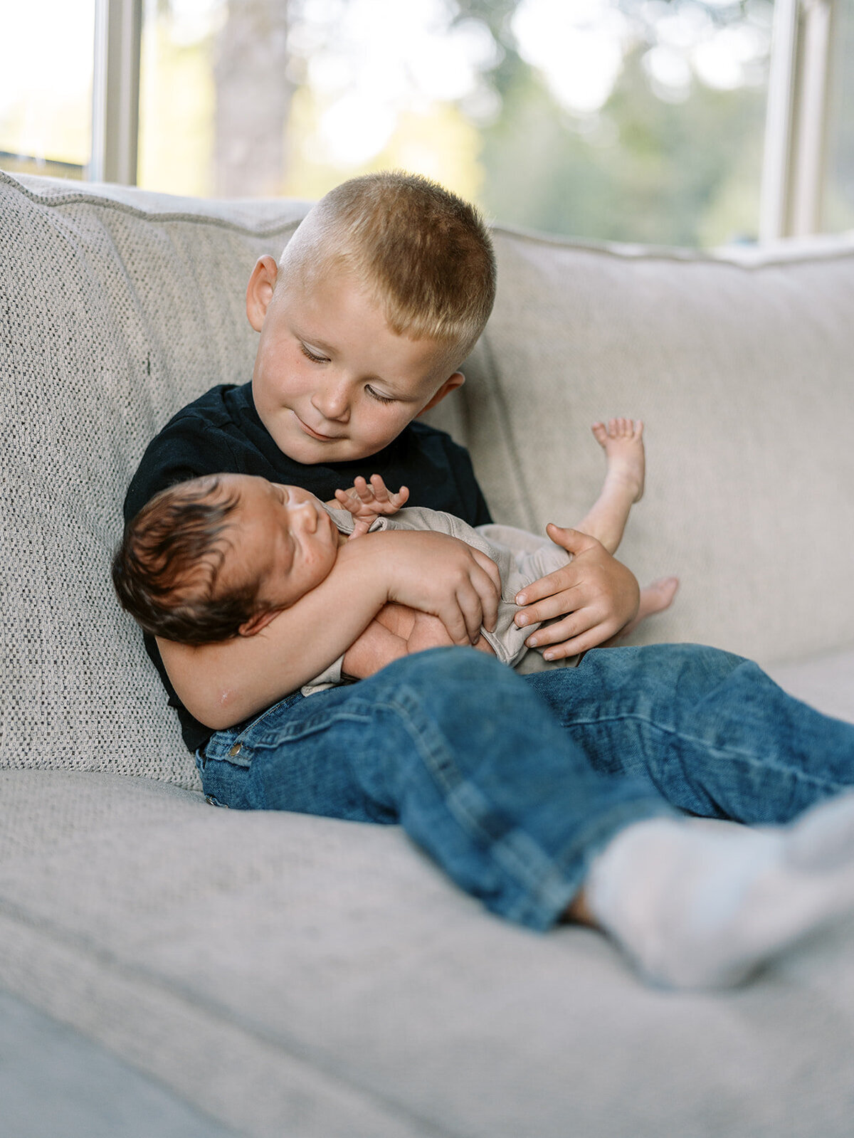 A young boy holds his baby sibling during at home photography session.