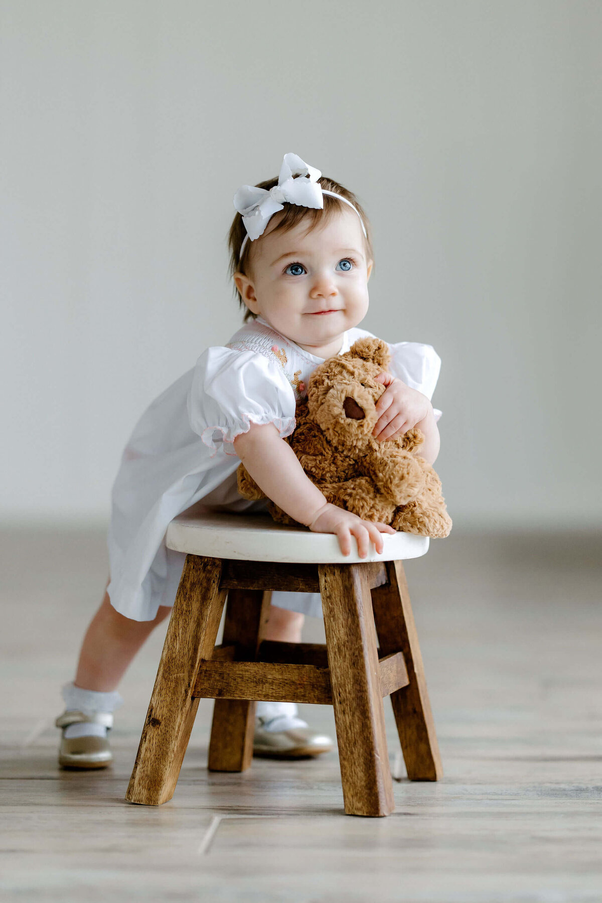 toddler girl in white dress holding stuffed bear on 1st birthday