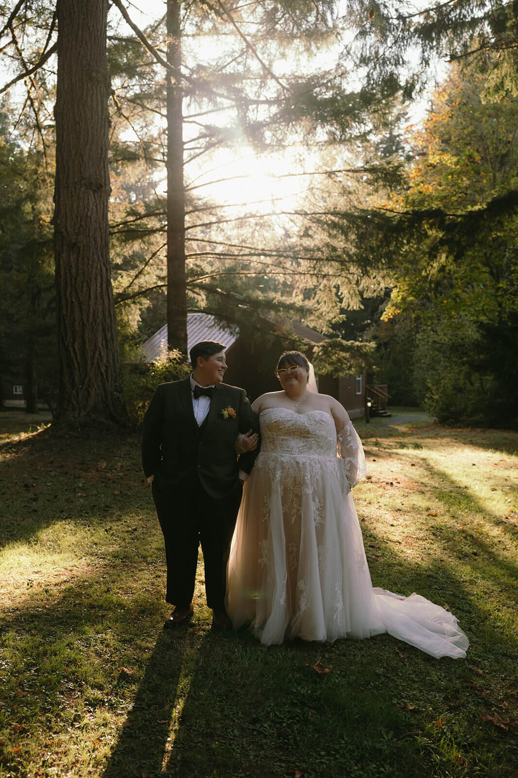Wedding couple stands next to each other with arms intertwined and smile their outdoor lake wedding.