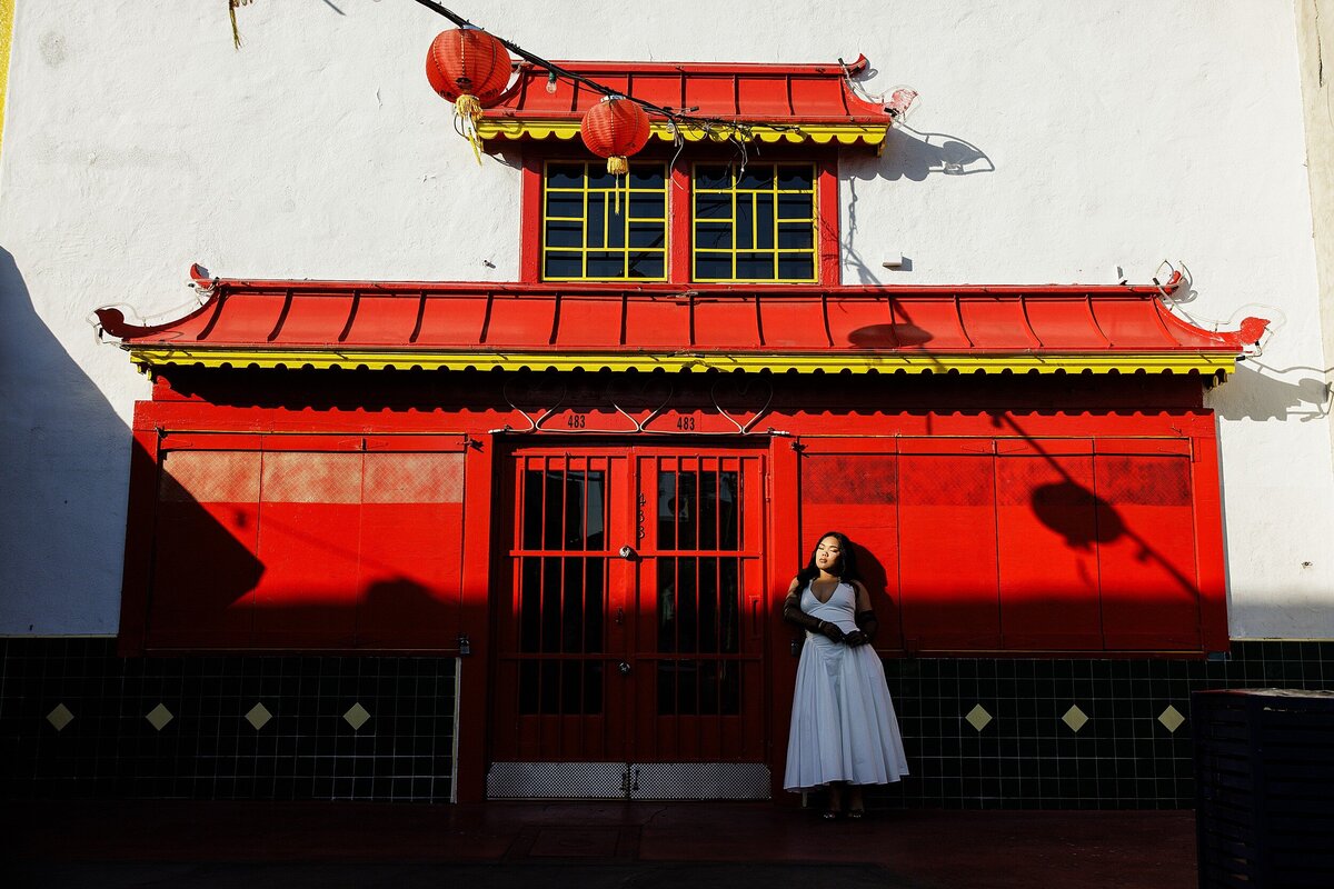 Editorial senior photo in front of bold red and gold Chinese architecture in Chinatown Los Angeles, featuring a dramatic white gown