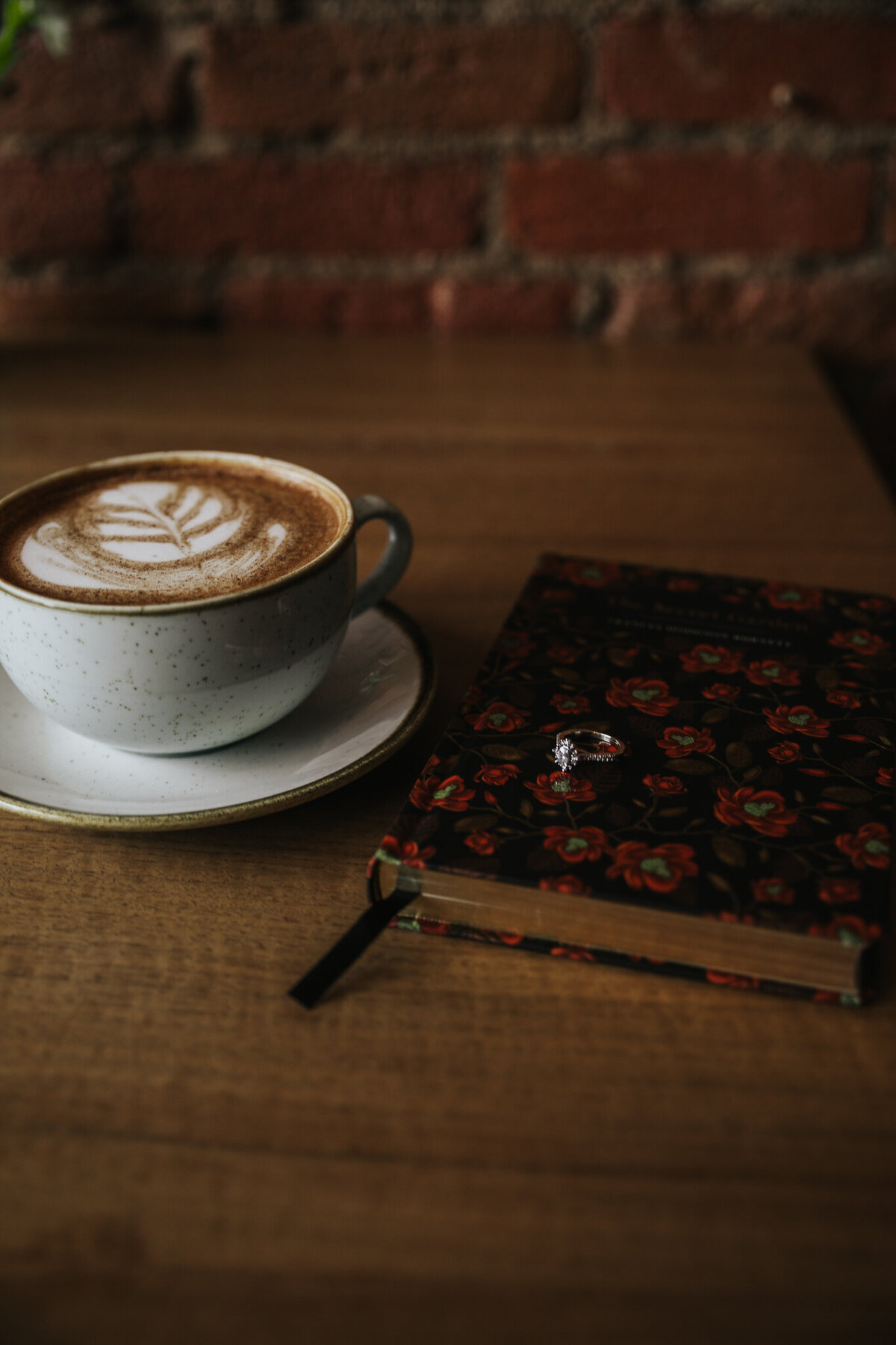 Engagement ring resting on floral book beside latte art at coffee shop in Valpraiso, IN during cozy couples photoshoot.