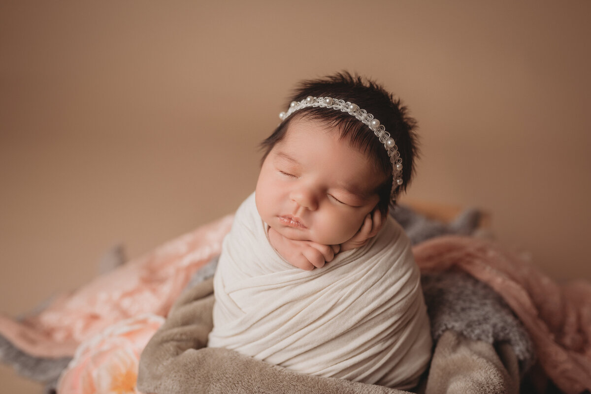 Newborn baby girl at Marietta GA portrait studio posed asleep and wrapped in white swaddle wearing pearl headband