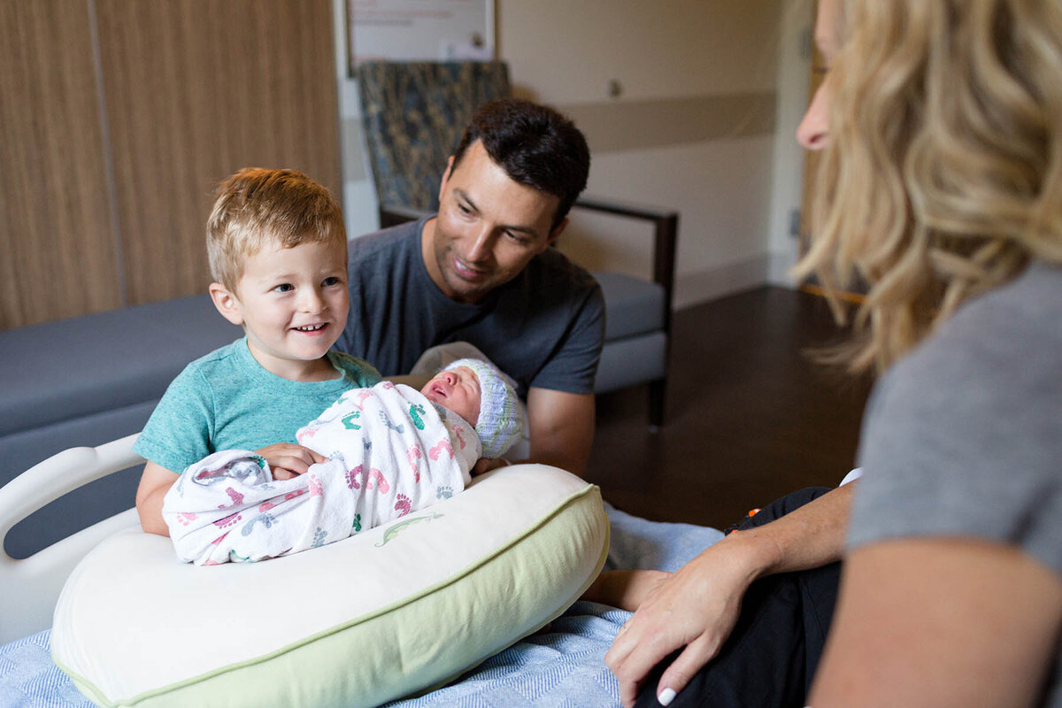 a big brother smiles proudly at his mother while holding his new baby brother