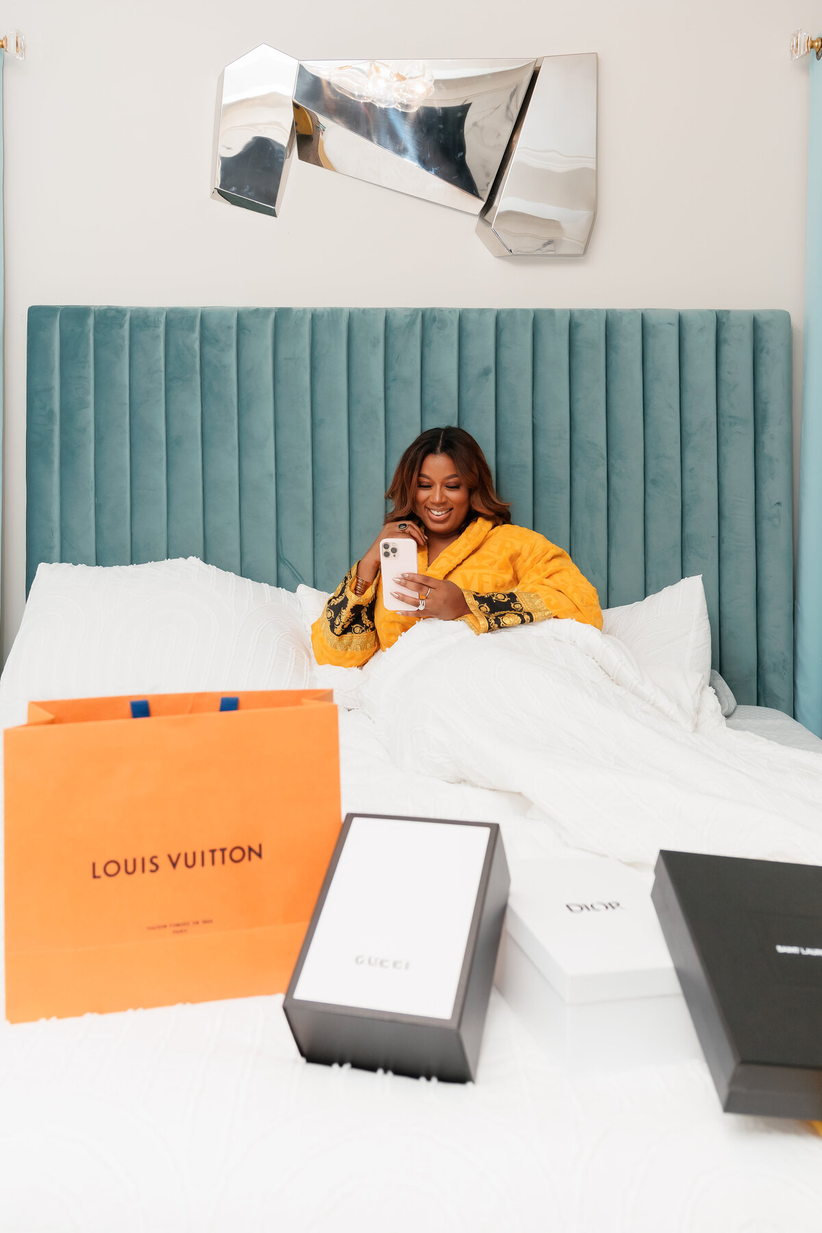 Luxury event planner poses with Louis Vuitton, Gucci bags in bed.