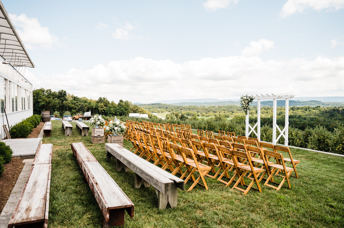 outdoor wedding ceremony set up at showalter's orchard with a large white wedding arch and warm toned foldable chairs with a stunning view of the Shenandoah mountains in the distance at showalter's orchard wedding venue