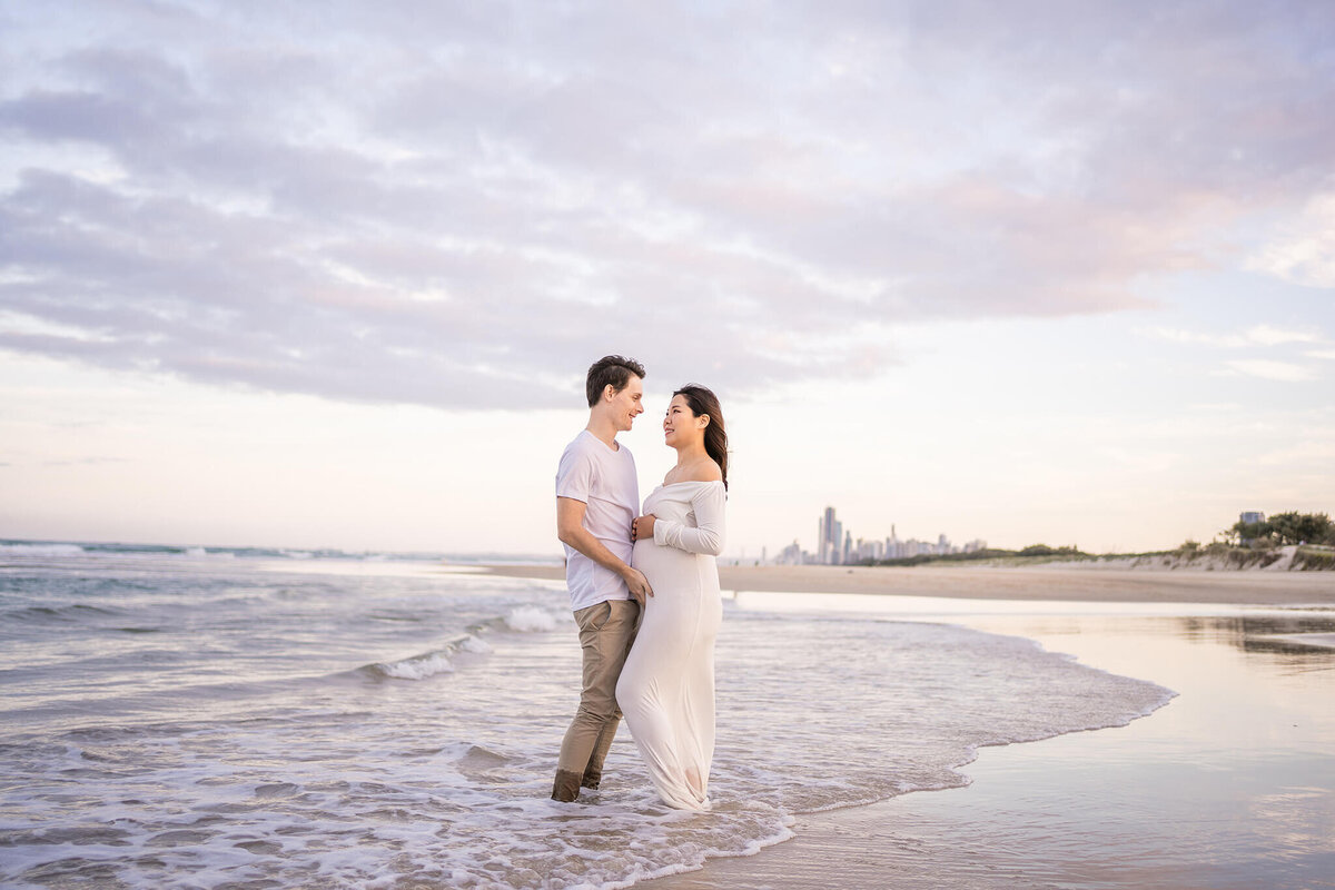 Couple posing for maternity photoshoot with Gold Coast city skyline during sunset in QLD