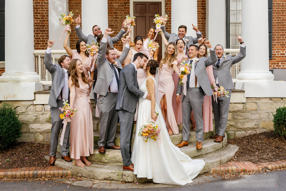 Bride and groom sharing exit kiss with guests cheering, Market Hall Raleigh celebration