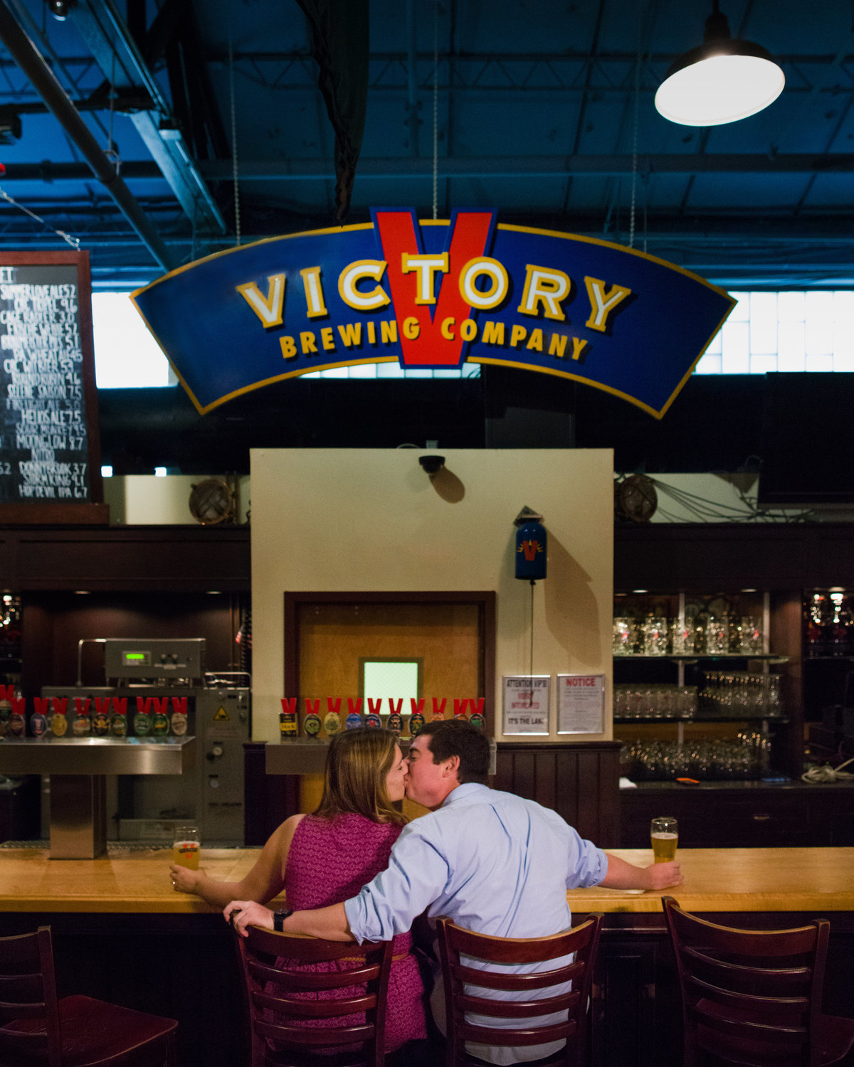 An engaged couple enjoying their engagement session at Victory Brewing Company brewery, sharing a relaxed and joyful moment surrounded by the unique charm of the brewery setting, filled with warmth and personality.