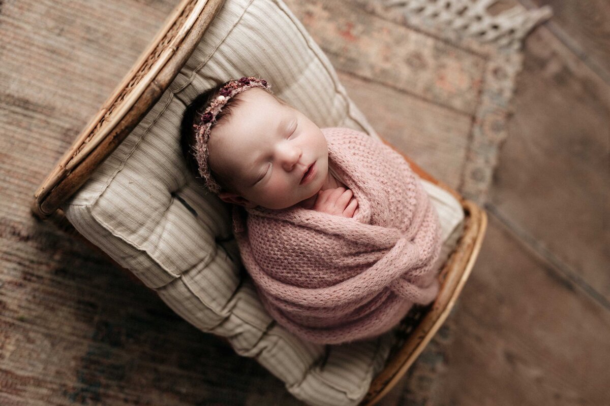 Studio newborn photography - sleeping baby girl swaddled in a pink newborn wrap on a newborn daybed.  Hands are folded under her chin.