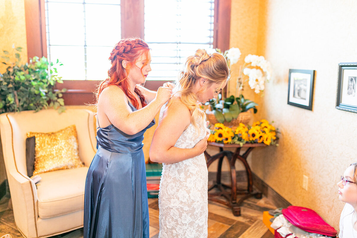 Maid of honor/sister getting the bride in her dress