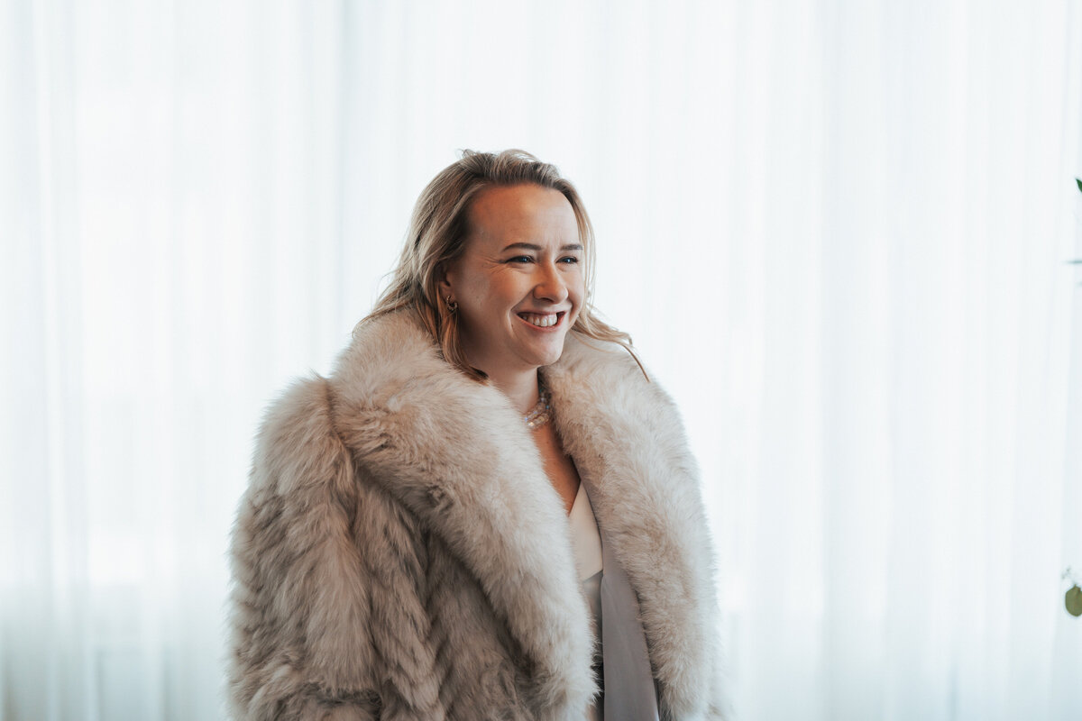 Woman wears a large fur coat at the altar of her winter elopement 