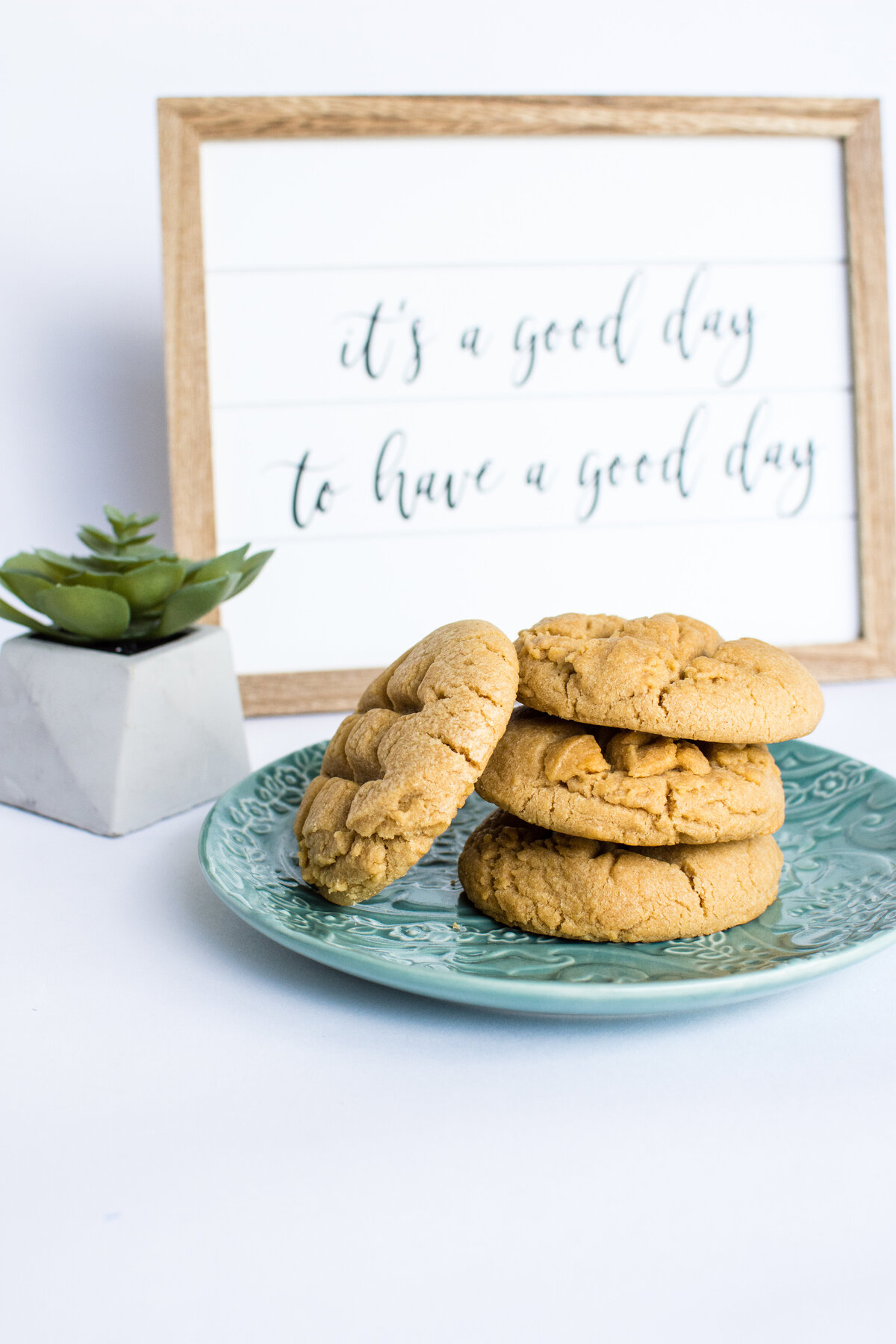 Peanut Butter cookies stacked on a green plate in front of a framed artwork that say "It's a good day to have a good day"
