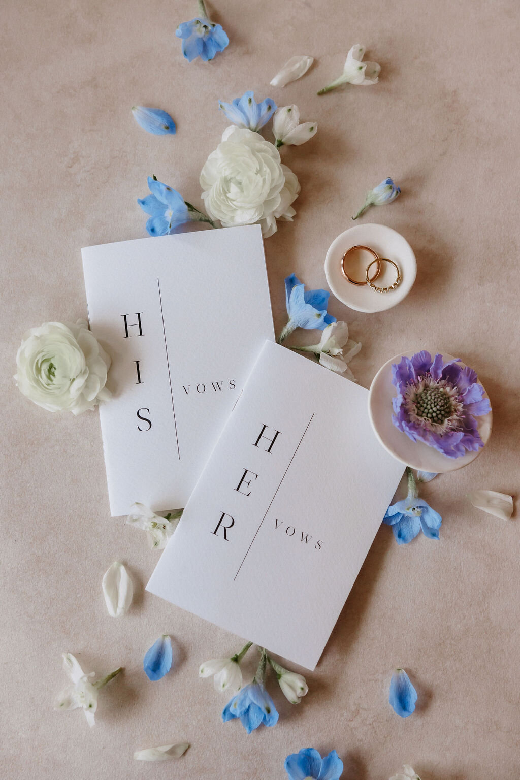His and hers vow books in a wedding flat lay with florals against neutral backdrop