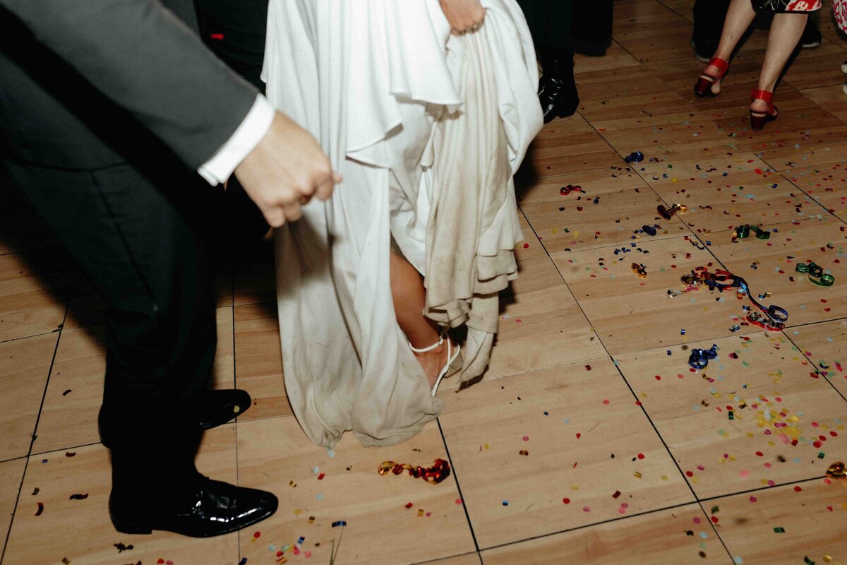 Close-up of bride and groom’s wedding attire on the dance floor with confetti scattered around