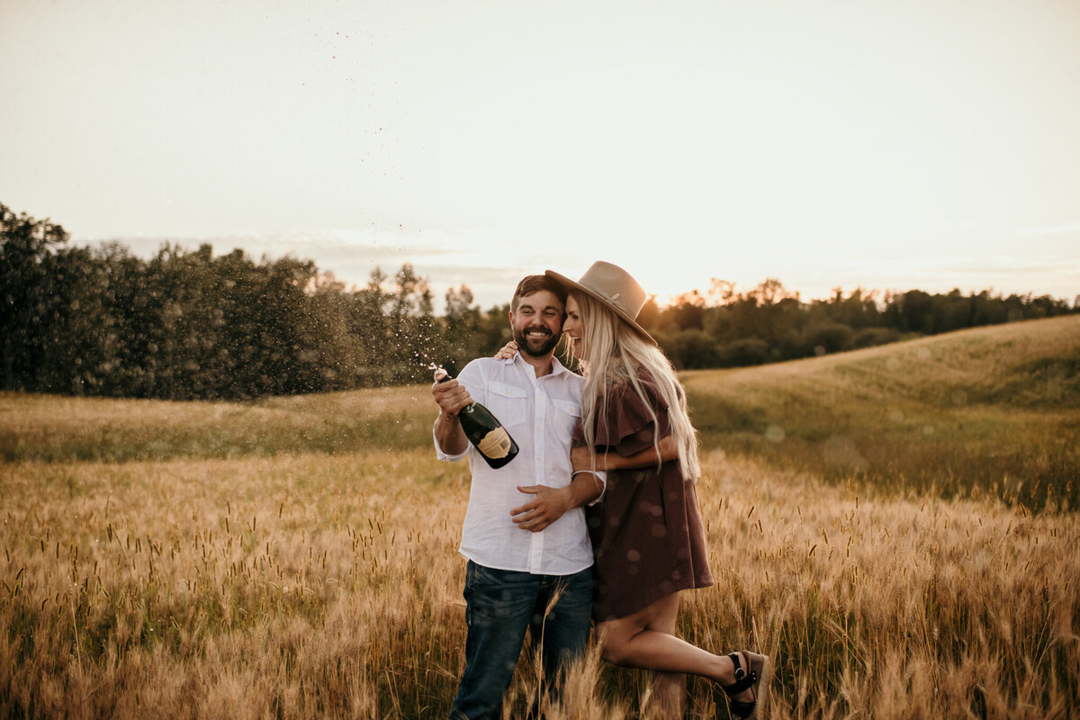 couple popping champagne in grass field
