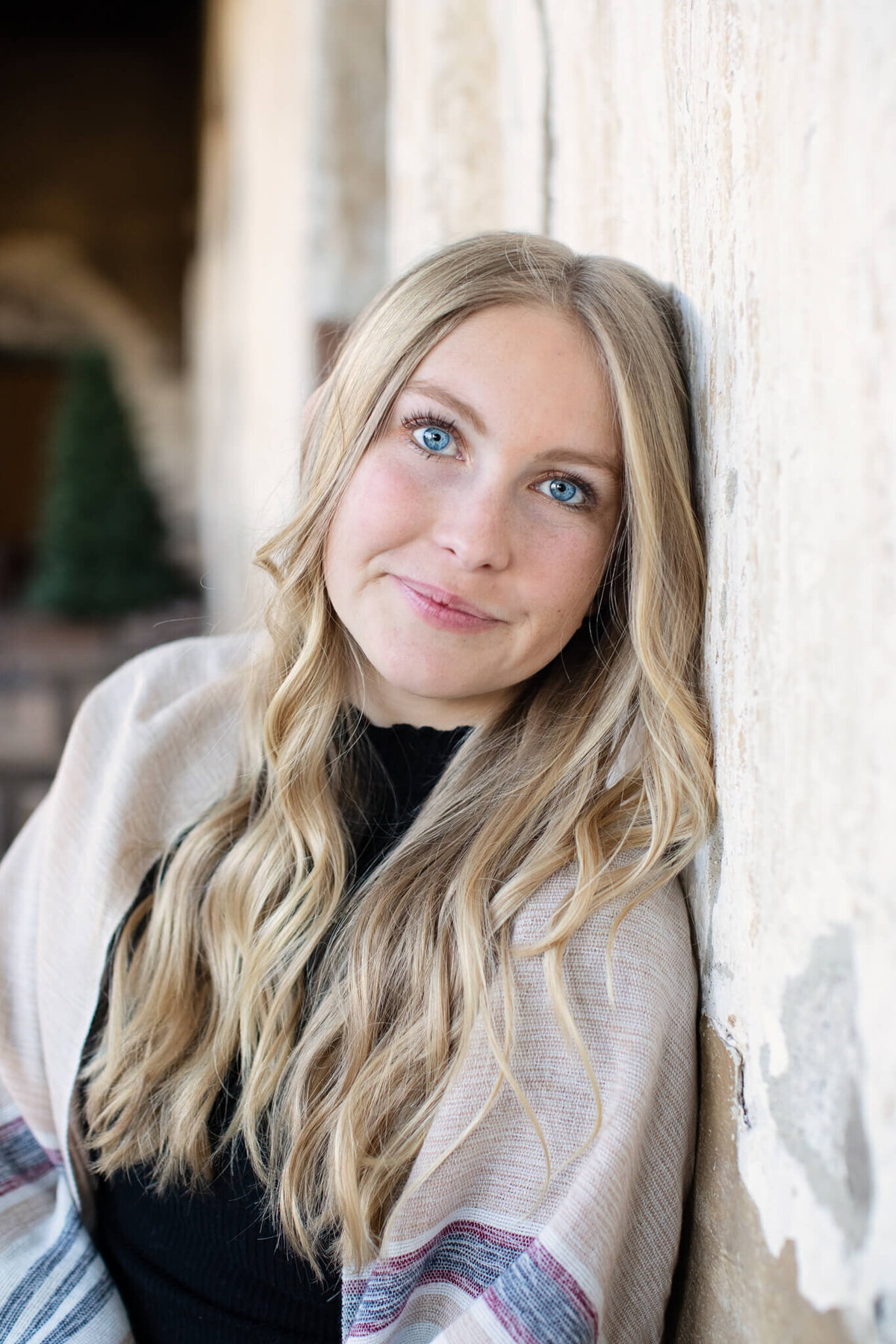 A close-up of a young woman with blue eyes and very blonde hair with her head against a wall, looking at the camera.