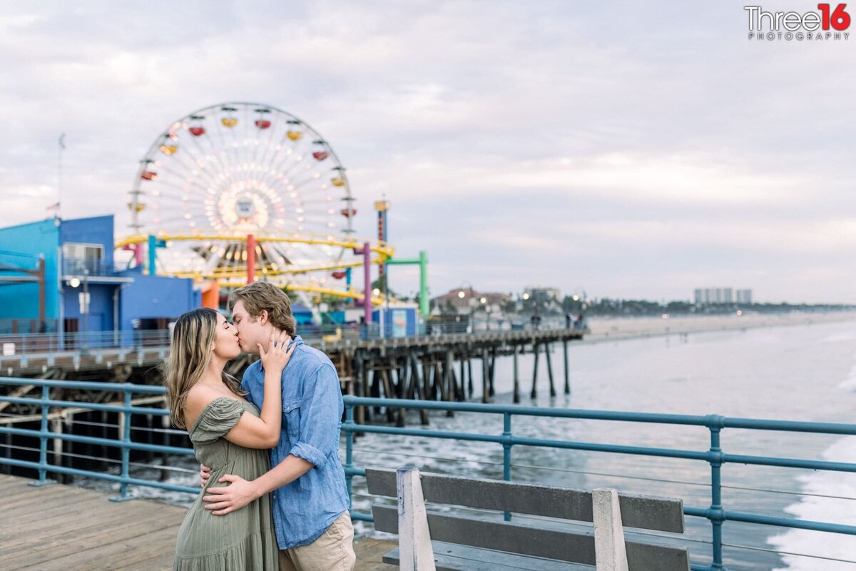 Engaged couple share a kiss with the Santa Monica Pier in the background