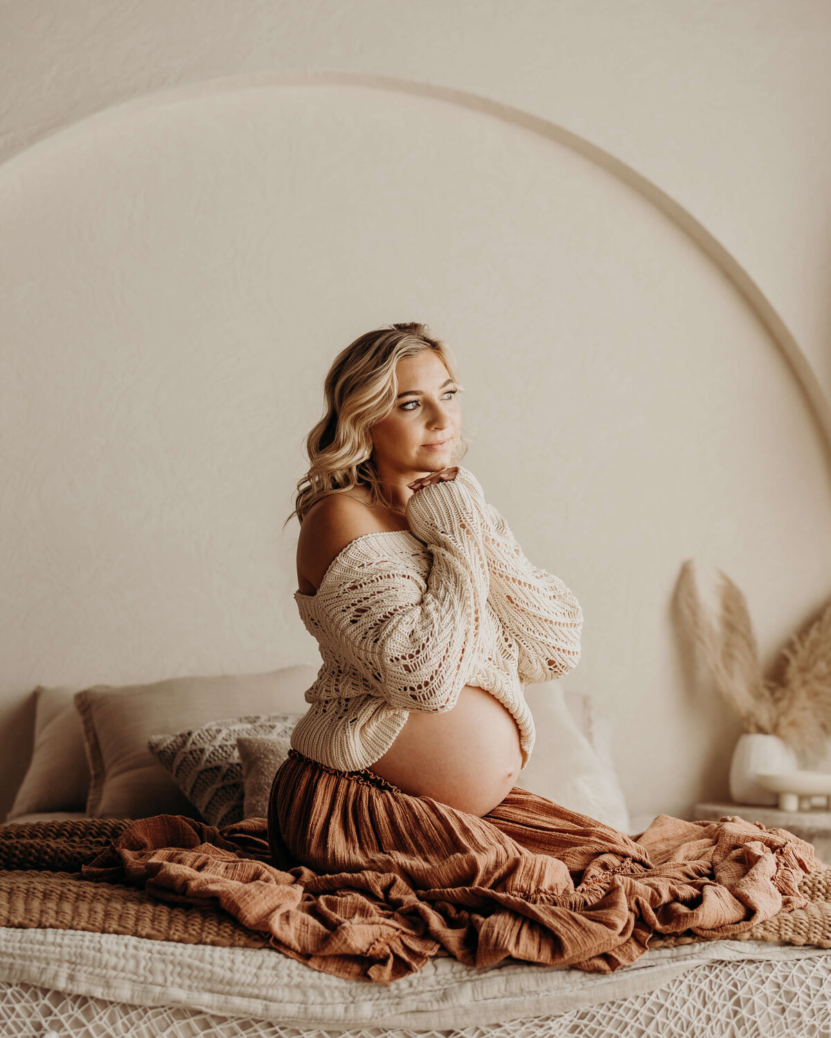 expectant mom kneels on bed while showing off baby bump