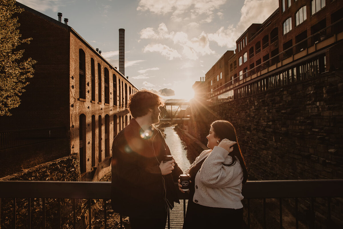 A couple standing on a bridge looking off over a river at sunset 