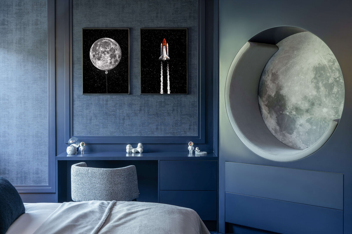 A navy blue wall with a built-in chair that looks like the moon. To the left are photos of the moon and a rocket, above a navy blue built-in desk.