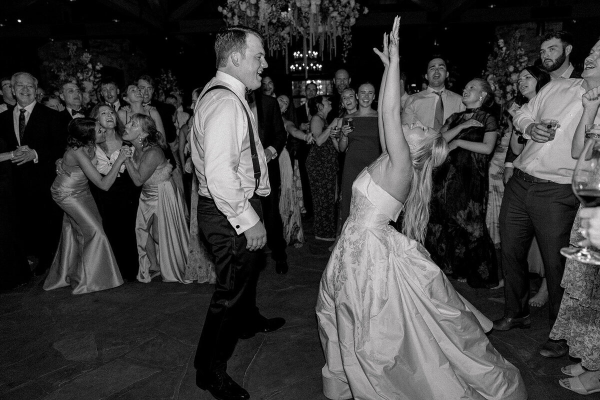 Black and white photo of bride and groom celebrating on the dance floor surrounded by cheering guests."