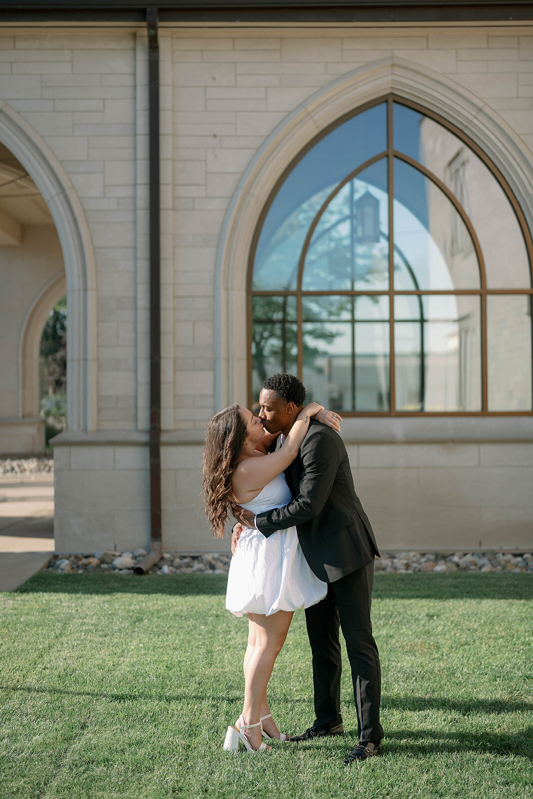 Exterior engagement portrait of couple embracing near tall arched windows in Kalamazoo.
