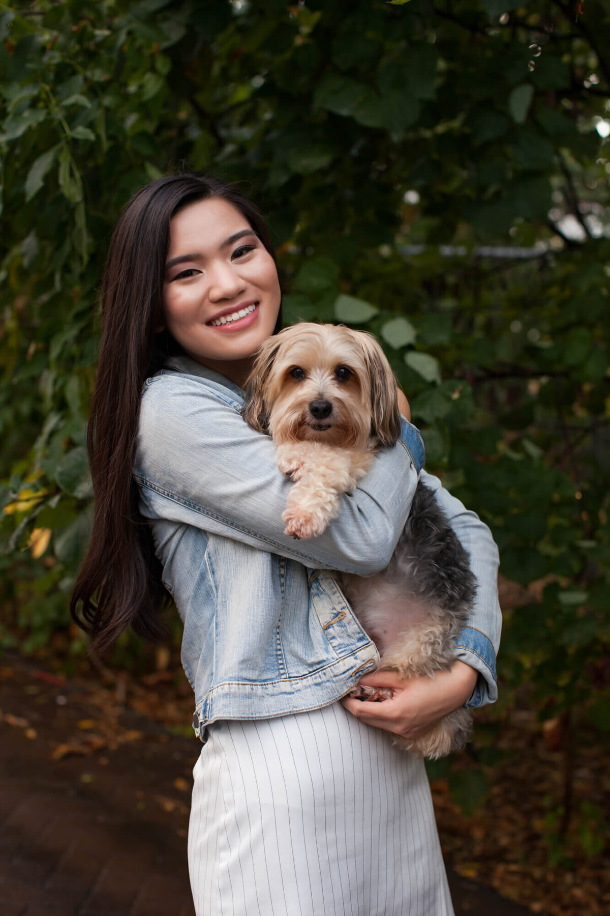 A lovely Asian American teen girl holds her small family dog in her senior portrait. Captured by Springfield, MO senior photographer Dynae Levingston.
