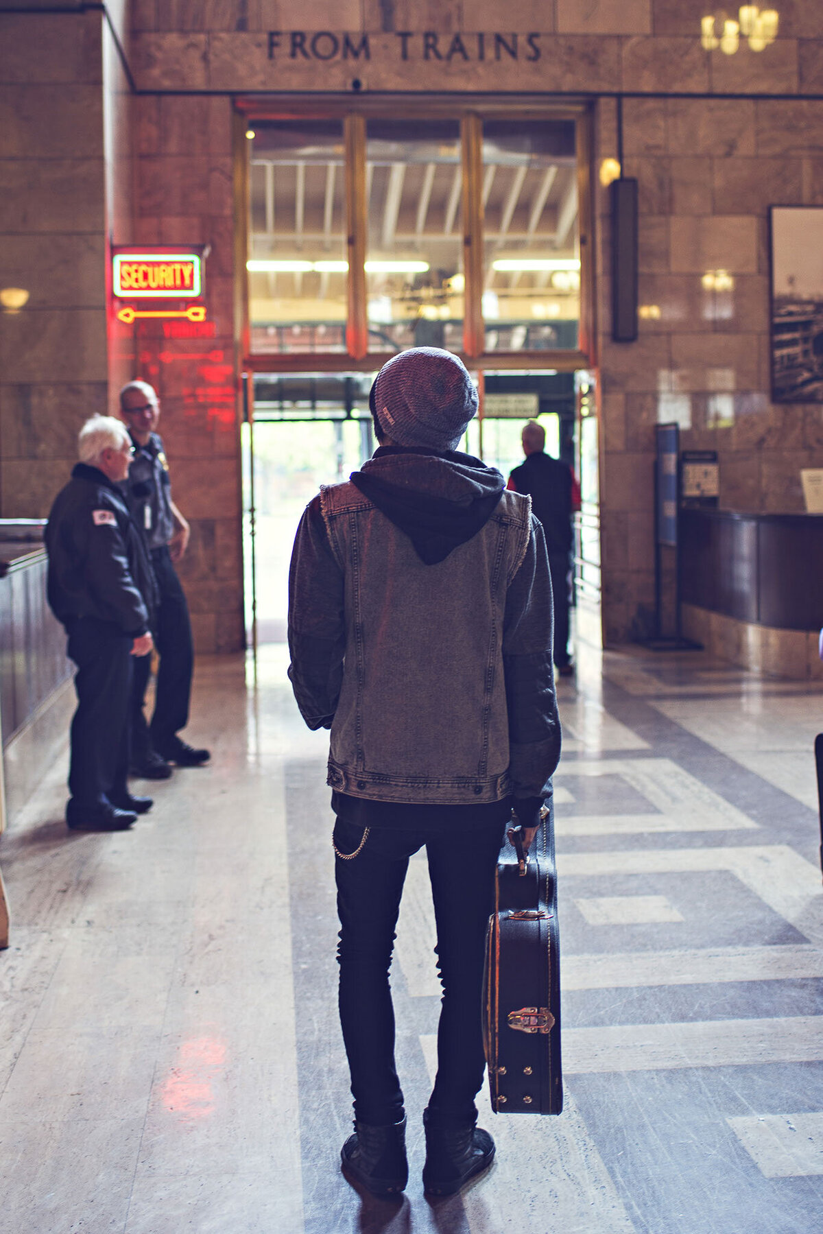 Guy walking in train station carrying guitar case