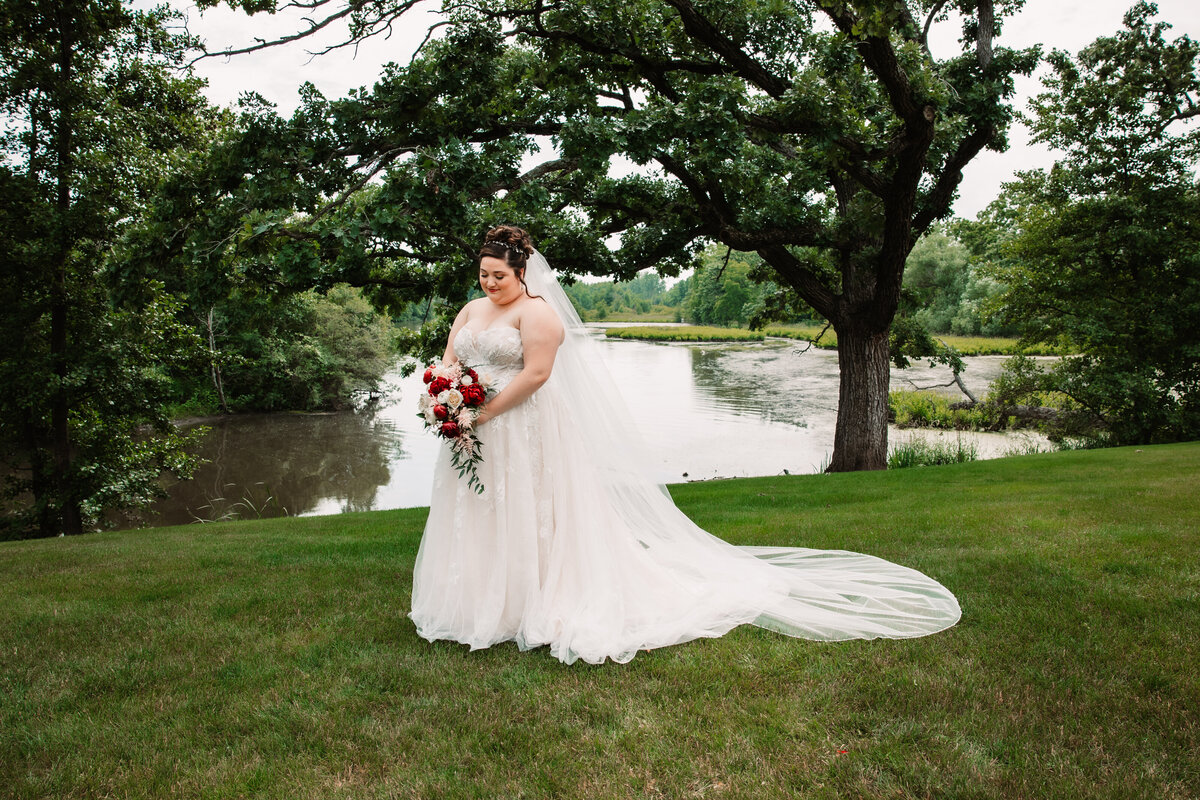 A bride stands in a lwn admiring her bouquet in her hands