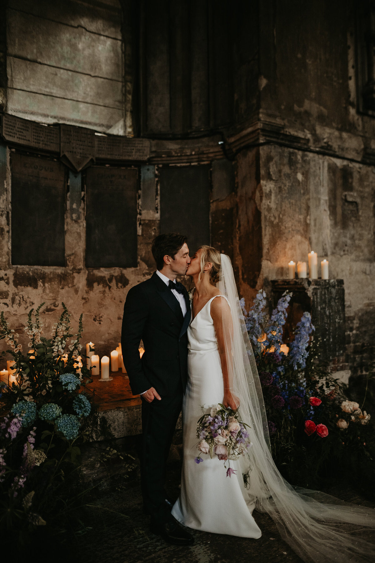 A bride and groom kiss whilst surrounded by candles and flowers at The Asylum Chapel in London. 