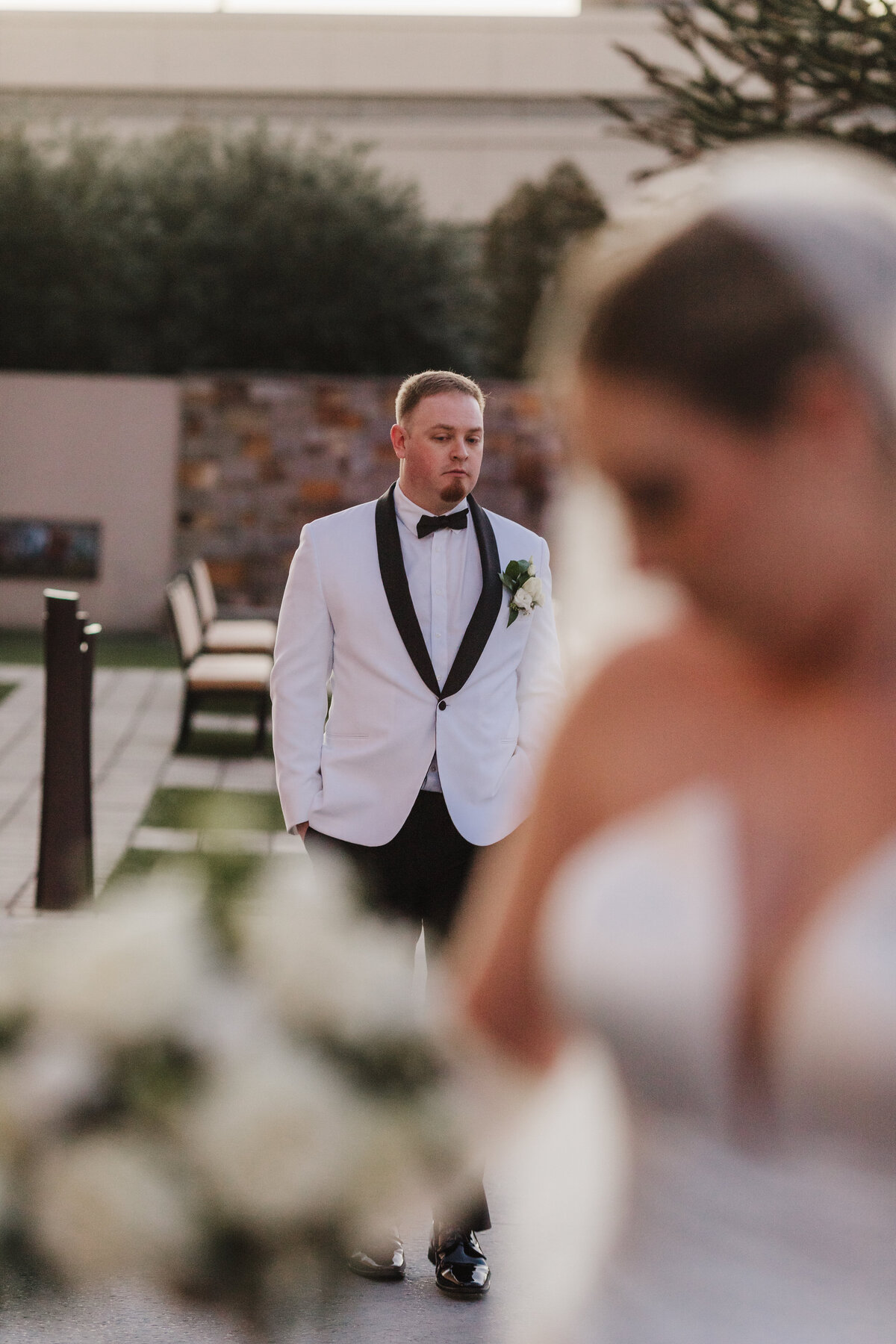 groom is captured in a candid moment in focus as the bride is in the foreground out of focus admiring her bouquet
