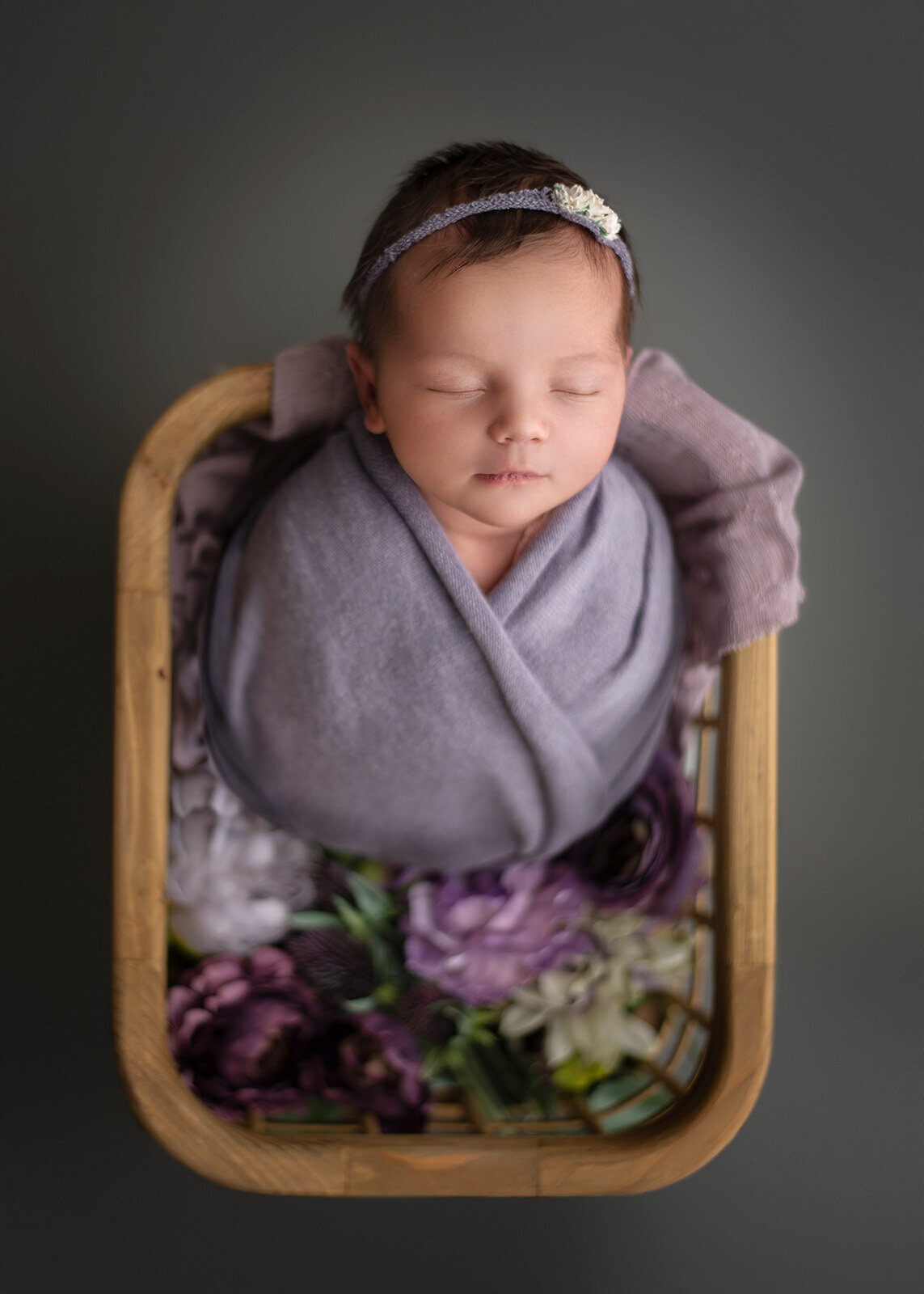 baby in a basket with flowers and purple blanket and headband