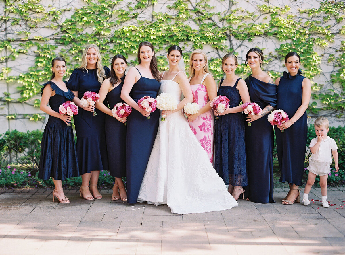 Bride with her bridesmaids, all smiling in navy dresses, holding pink and white bouquets.